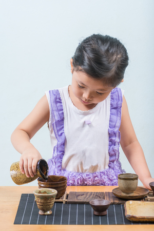 Cute Asian Girl While playing a cup of tea and a cup of sake. the intention is to practice the meditation of the children at home.の写真素材