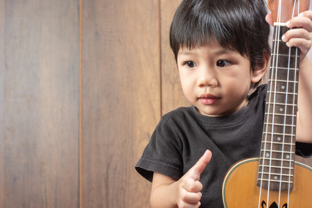 Portrait of cute Little Boy playing Ukulele of musical instruments. on wooden background, funny concept. with space for text.の写真素材