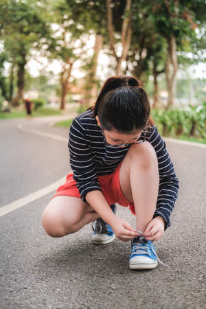 Runner little Asian girl in Park, getting ready for run tying laces of running shoes.の写真素材