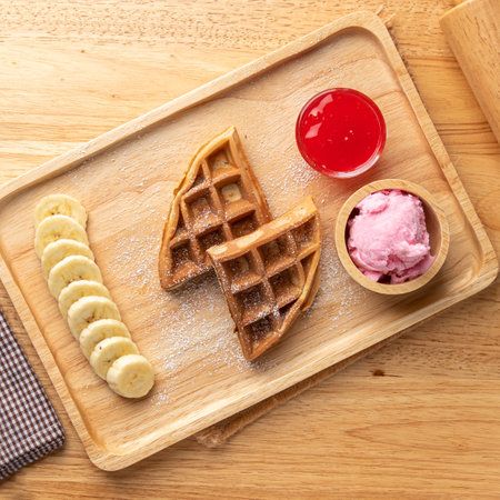 Top Table View of Hot waffles topped with icing and jam, banana and cake are a perfect side dish on a wooden tray.の写真素材