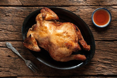 Delicious golden roasted chicken on a vintage black plate With sweet chicken dipping sauce, and a fork in natural evening light.の写真素材