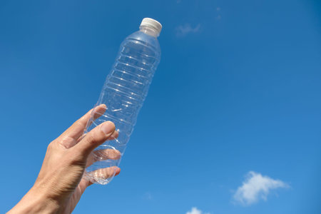 Close up Man's hand holding a bottle of water with blue sky background with copy space for your...