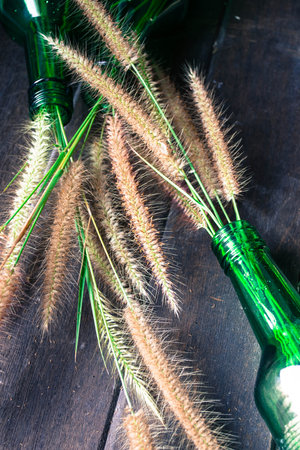 Grass in green glass bottles on the wooden background