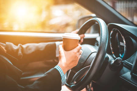 Business woman's hand holding a coffee cup to take away, she is driving in the morningの写真素材