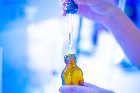 hands active substance is added dropwise with pipette and glass flask in laboratoryの写真素材