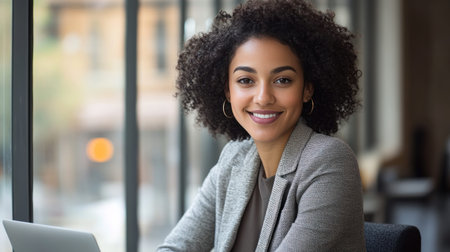 African American woman with curly hair is sitting at a table with a laptop in front of her...の素材