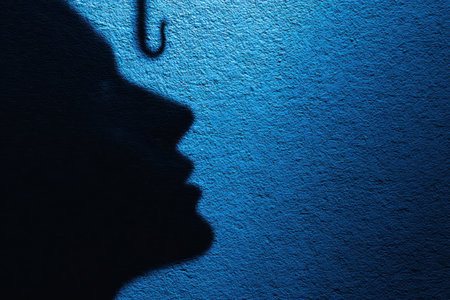 Shadow of person facing phishing hook on textured blue wall symbolizing email phishing protection and online security awareness.の素材