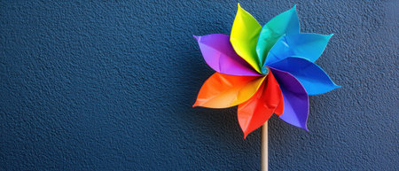A Colorful pinwheel spinning against blue wall, proud symbol of joy and playfulnessの素材