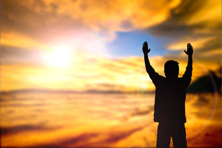 Silhouette of man with raised hands over blur cross concept for religion, worship, prayer and praise.の写真素材