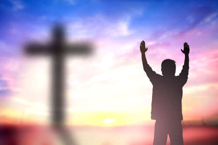 Silhouette of man with raised hands over blur cross concept for religion, worship, prayer and praise.の写真素材