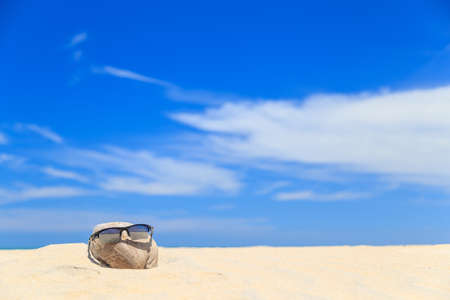 Sunglasses over coconut fruit on sandy beach under hot shiny sun light looked like a happy (tourist) man lying on the beach during holiday summer vacation on wonderful trip under bright blue sky.の写真素材