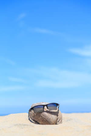 Sunglasses over coconut fruit on sandy beach under hot shiny sun light looked like a happy (tourist) man lying on the beach during holiday summer vacation on wonderful trip under bright blue sky.の写真素材