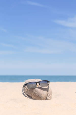Sunglasses over coconut fruit on sandy beach under hot shiny sun light looked like a happy (tourist) man lying on the beach during holiday summer vacation on wonderful trip under bright blue sky.の写真素材