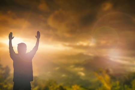 Silhouette of man with raised hands over blur cross concept for religion, worship, prayer and praise.の写真素材