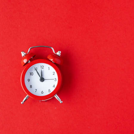 Creative flat lay vintage clock on red office table top view background concept alarm clock on red paper color with copy space in minimal style, empty template for text, break workplace at noon for lunch, back to school.の写真素材