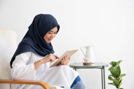 Young Muslim women Students is a creative freelance journalist sit writing to be entrepreneur job concept for hijab girl Islam religion Asian ethnic joyful internet banking on tablet mobile smartphoneの写真素材