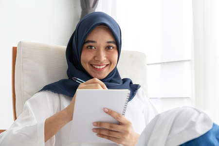 Young Muslim women Students is a creative freelance journalist sit writing to be entrepreneur job concept for hijab girl Islam religion Asian ethnic joyful internet banking on tablet mobile smartphoneの写真素材