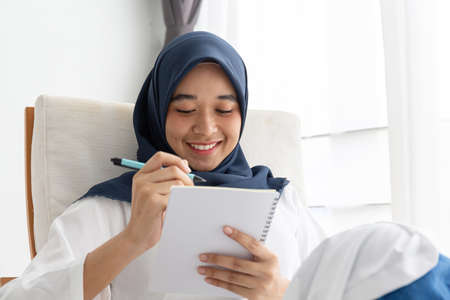 Young Muslim women Students is a creative freelance journalist sit writing to be entrepreneur job concept for hijab girl Islam religion Asian ethnic joyful internet banking on tablet mobile smartphoneの写真素材