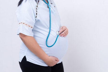 Pregnant woman in blue dress holds belly on a white background. close up of happy pregnancy hands...