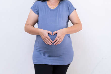 Pregnant woman in blue dress holds belly on a white background. close up of happy pregnancy hands touch on tummy healthy concept. motherhood stand wait for childbirth in hospital.の写真素材