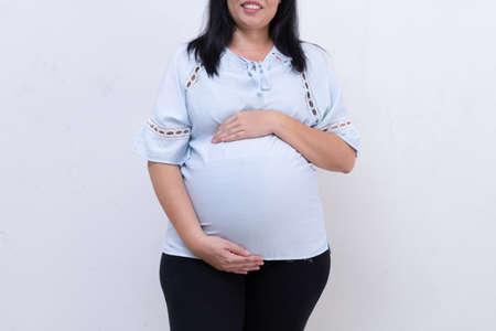 Pregnant woman in blue dress holds belly on a white background. close up of happy pregnancy hands touch on tummy healthy concept. motherhood stand wait for childbirth in hospital.の写真素材