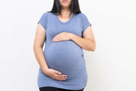 Pregnant woman in blue dress holds belly on a white background. close up of happy pregnancy hands touch on tummy healthy concept. motherhood stand wait for childbirth in hospital.の写真素材