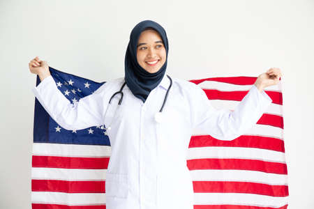 Young Muslim women exchange Students scholarship wear holding america flag over white background concept for hijab girl Islam religion Asian happy in united stage independent day cultureの写真素材