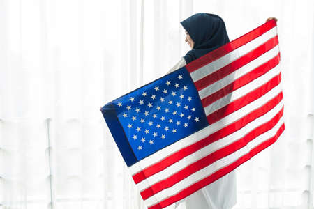 Young Muslim women exchange Students scholarship wear holding america flag over white background concept for hijab girl Islam religion Asian happy in united stage independent day cultureの写真素材