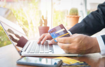 Business man hand hold credit card to shopping internet online bill on computer, Debit saving purchase buy on table background. Shopaholic people retail pay sale money, bank terminal account conceptの写真素材