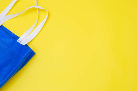 Flat lay eco blue shopping bag on paper yellow color background for tote present reduce mock up stuff shop. Linen canvas textile cloth sale on table top view, care world plastic free reusable concept.の写真素材