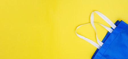 Flat lay eco blue shopping bag on paper yellow color background for tote present reduce mock up stuff shop. Linen canvas textile cloth sale on table top view, care world plastic free reusable concept.の写真素材