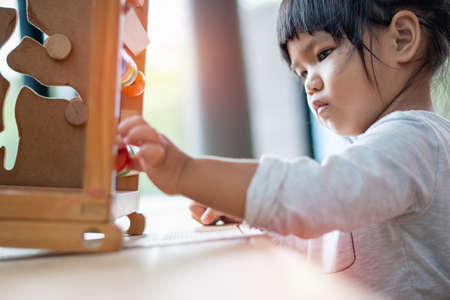 Kids learnfrom play with colourful wooden toy on table top at home. Preschool young girl concentrate with educational equipment in recess term back to school Children at home or daycare kindergarten.の写真素材