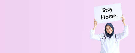 Young Arab Muslim doctor women smile showing white card on pink background concept for Islam people working in medical hospital health care, Modern Nurse wear hijab in pandemic stay home text.の写真素材