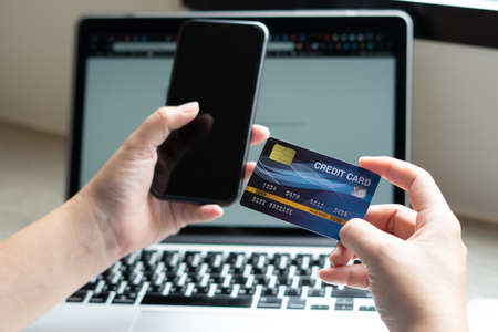 Business woman hand hold credit card to shopping internet online bill on computer, Debit saving purchase buy on table background. Shopaholic people retail pay sale money, bank terminal account conceptの写真素材