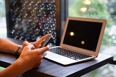 Young entrepreneur SME use notebook showing blank screen with clipping path display  in cafe concept.Â Hand of business man hold smartphone People use 5G cellular work app with modern internet of thingsの写真素材