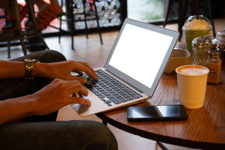 Young entrepreneur SME use notebook showing blank screen with clipping path display  in cafe concept.Â Hand of business man hold smartphone People use 5G cellular work app with modern internet of thingsの写真素材