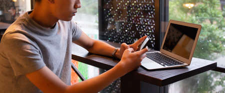 Young entrepreneur SME use notebook showing blank screen with clipping path display  in cafe concept.Â Hand of business man hold smartphone People use 5G cellular work app with modern internet of thingsの写真素材