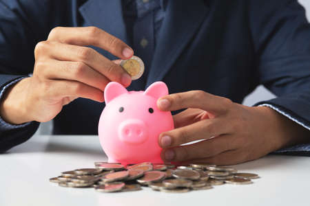 Hand of Business man holding coin put in piggy bank with money stack growing growth saving money, Concept invesment for financial freedom plan, business deposit to hope successの写真素材