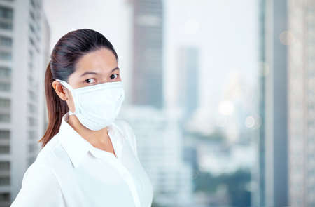 Young woman in safety medical mask in home isolation on blur outside office window view self business quarantine conceptの写真素材