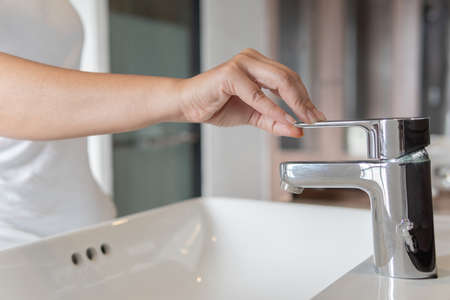 Close up Woman with chrome faucet washbasinの写真素材