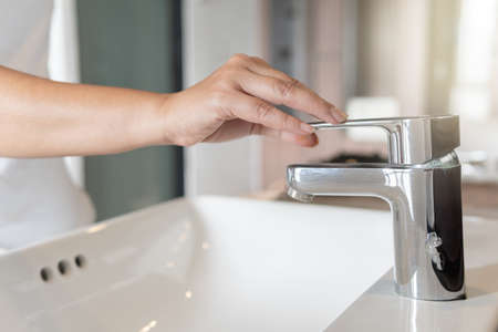 Close up Woman open chrome faucet washbasin to washing hands rubbing with soap for corona virus at water tap. Faucet and water drop off. Bathroom interior with sink basin and water tap.の写真素材