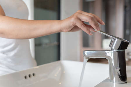Close up Woman open chrome faucet washbasin to washing hands rubbing with soap for corona virus at water tap. Faucet and water drop off. Bathroom interior with sink basin and water tap.の写真素材