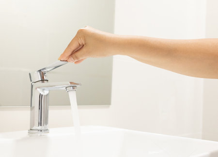 close up Woman open pull chrome faucet washbasin to washing hand soap for corona virus at water tap. push off water running drop off. Bathroom interior background with sink basin faucet tap.の写真素材