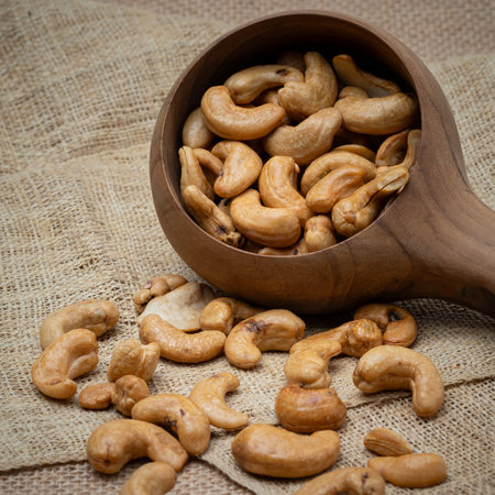 Roasted cashew nuts and halves in wooden bowl on table top view. Macro studio shot Homemade Roasted Salted Cashews in basket and spoon breakfast on sack, Healthy food Seeds snack productの写真素材