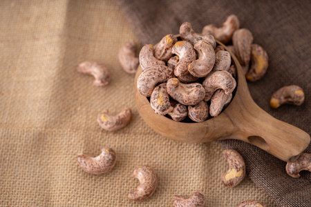 Roasted cashew nuts and halves in wooden bowl on table top view. Macro studio shot Homemade Roasted Salted Cashews in basket and spoon breakfast on sack, Healthy food Seeds snack productの写真素材