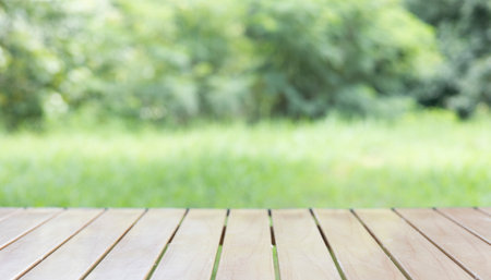 Wood table in outdoor setting lush green grass on lawn. smooth, clean planks under the bright sunlight, reflection polished surface, the natural texture in this peaceful scene of backyard nature.の写真素材