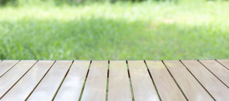 Wood table in outdoor setting lush green grass on lawn. smooth, clean planks under the bright sunlight, reflection polished surface, the natural texture in this peaceful scene of backyard nature.の写真素材