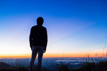 Silhouette of Man in hood standing on top of mountain waiting for sun riseの写真素材