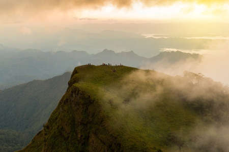 people hiking to top of mountain with flowing mist and beautiful sunsetの写真素材