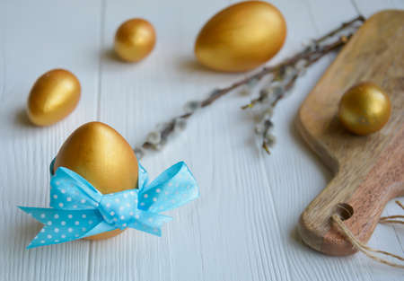 Easter. Easter eggs of chicken and quail gold color and branches of vreba on a white wooden background with space for text.の写真素材